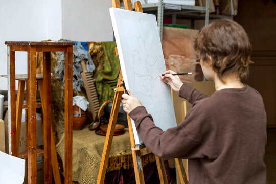 A female artist paints a still life from life. An easel with a sketch in an art studio. 