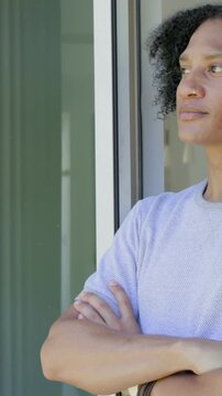 Vertical video: Camera zooming man in light shirt crossing arms, gazing at window showing nose ring