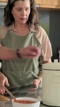 Vertical video: Reading tablet, woman in apron making sauce at counter with bowl and lidded jar