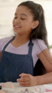Vertical video: Smiling apron girl seeing offscreen hand offering bottle, helping bake in kitchen