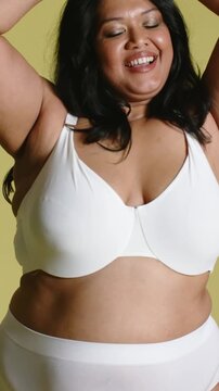 Vertical video: Frame widening, model raising arms, swaying on pale set, showing white bra briefs