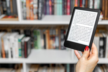 a woman's hand holding an e-book. A woman reads an e-reader near a bookcase. an e-book against the background of paper books. A woman reading an e-book at home. isolate of a hand holding an e-book © Oleg Opryshko