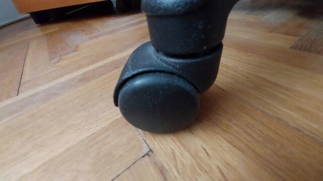 Office chair caster wheel rolling on parquet floor close up
