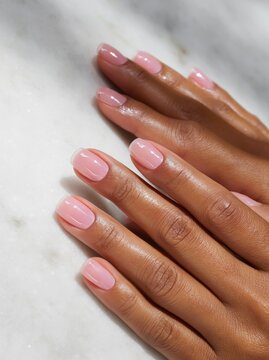 Close up of female hands with short squoval nails featuring a light pink polish resting on a marble surface, showcasing well-groomed fingers and natural skin tone