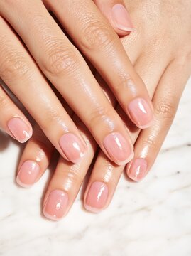 Close up of female hands with short squoval nails painted in light pink color resting on a marble surface, showcasing well-groomed fingers and polished nails