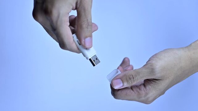 Hands removing the protective cap from a white USB flash drive against a plain light background.