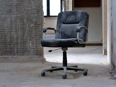  dusty black office chair sitting in the middle of a
room under renovation. The chair, showing signs of wear and age, is positioned
on a raw concrete floor. In the backgrod