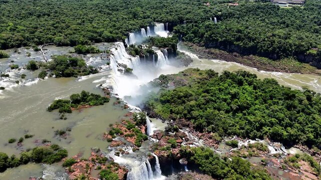 Aerial drone footage of the majestic Iguazu Falls with a view toward the Argentine side. A breathtaking panorama of powerful cascading waterfalls surrounded by lush tropical rainforest. 