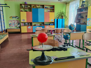 A bright and colorful elementary school classroom during the holidays, featuring educational materials, desks, and geographical models, including globes and teaching aids for studying the solar system © Віталій Чибиряк
