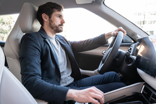 Businessman driving modern electric car in bright city daylight