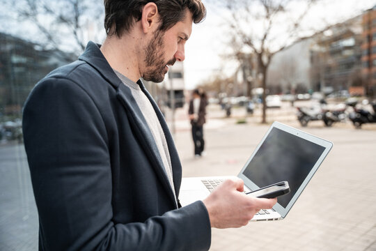 Business man using smartphone and laptop outside office
