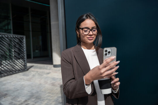 Businesswoman in blazer using smartphone against blue wall