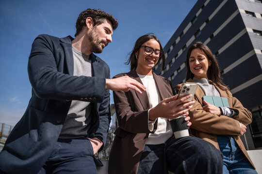Colleagues outdoors checking smartphone near modern office