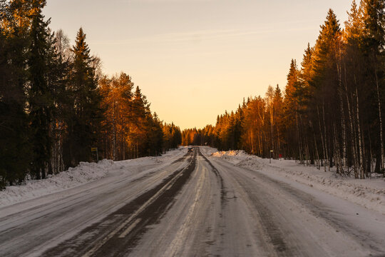Winter road through snowy forest at sunset in Finland