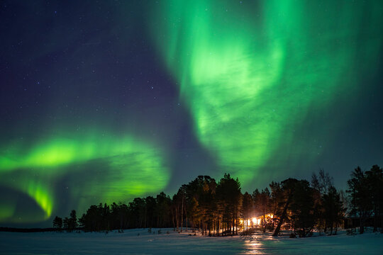 Northern lights over snowy forest and cabin in Finland