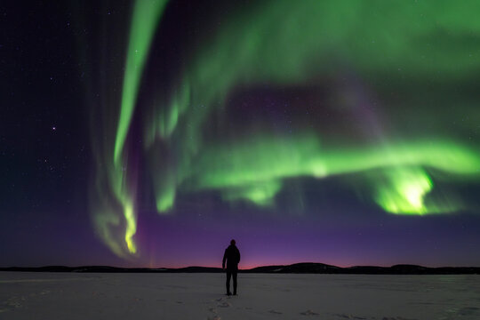 Northern lights over frozen lake with lone traveler, Finland