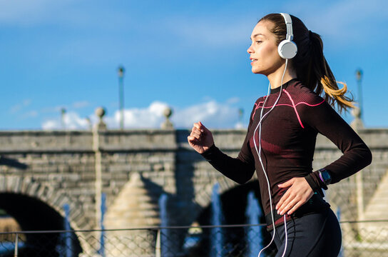 Woman jogging with headphones near historic bridge