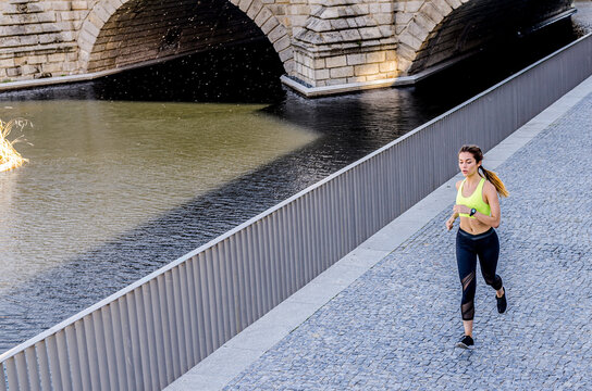 Woman running along riverside cobblestone path