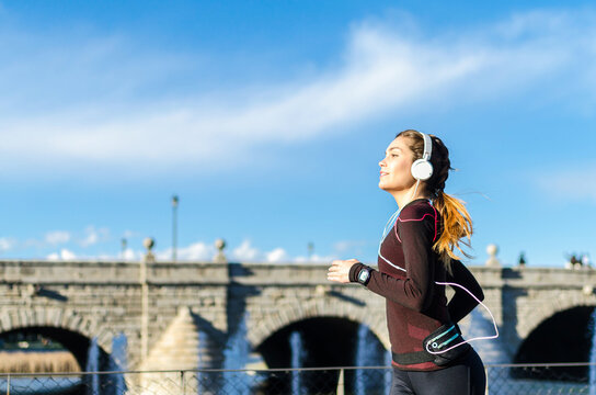 Woman running with headphones near stone bridge
