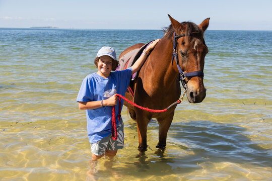 smiling young boy posing with horse at edge of ocean,Mozambique, Africa