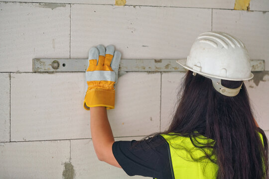 Female construction worker checking white aac bricks with horizontal level, view form behind, face not visible