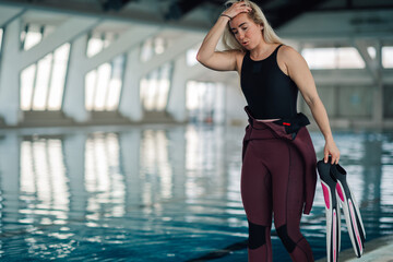 Tired woman catching breath after intense swimming workout, wearing wetsuit and flippers at indoor pool © Zamrznuti tonovi