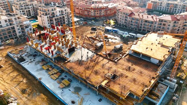 Top down view of concrete pouring process on construction site. High angle view of workers pouring concrete for a foundation slab with two concrete pump trucks and cranes.