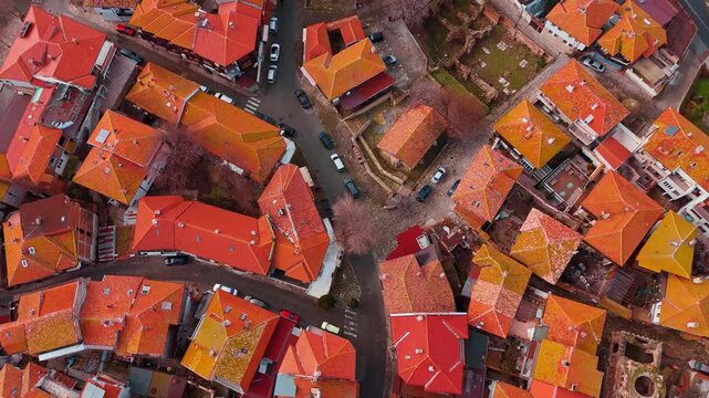 Top view of red tiled roofs and ancient ruins. Aerial downward perspective of historic town buildings and stone archeological ruins between houses.