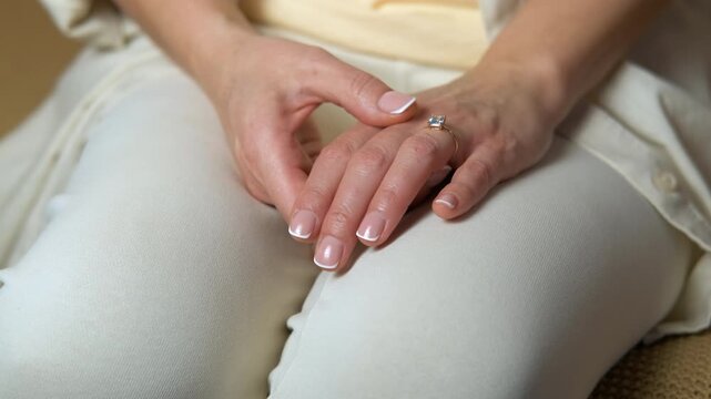 Woman nervously fidgeting with her engagement ring. Close-up of a woman's hands with a beautiful french manicure as she sits with them clasped on her lap, anxiously fidgeting with the engagement ring