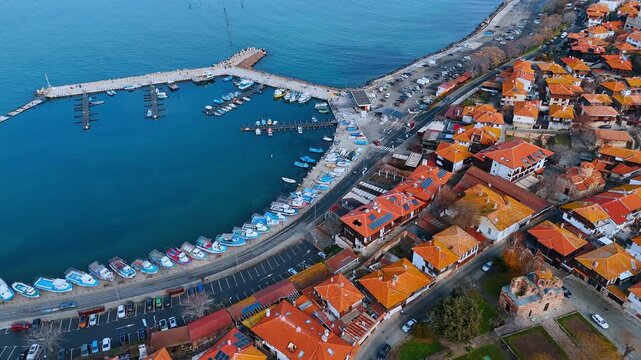 Wide aerial shot of fishing harbor and red roofs. Many small boats docked in a curved harbor next to traditional houses.