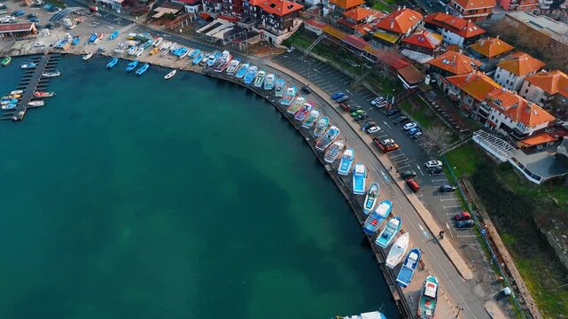 Curved harbor view with fishing boats and parking. Aerial shot of rows of small boats moored along a quay with a parking lot.