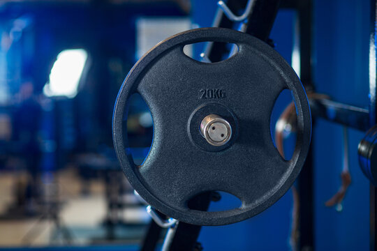 Weight plate with 20kg marking on gym rack with industrial interior and blue accent lighting