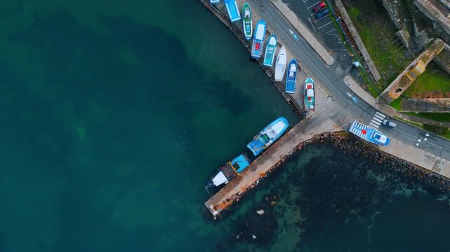 Top down view of colorful fishing boats at pier. Small wooden fishing boats moored at a concrete pier in clear green water.