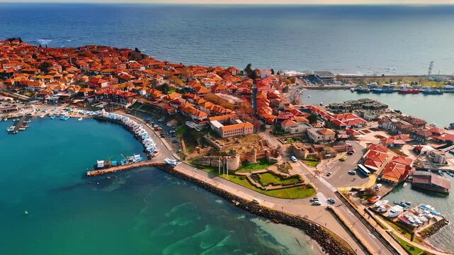 High angle view of historic coastal peninsula with ancient ruins. Aerial perspective of town on peninsula featuring red tile roofs, stone ruins, and turquoise sea water.