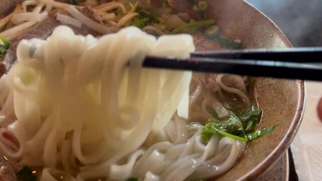 Eating ramen noodles pho bo dish at vietnamese restaurant with chopsticks