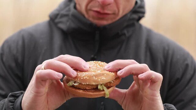Man eating burger outdoors, enjoying fast food during picnic in nature. Concept of casual lifestyle, comfort food and outdoor eating.