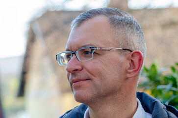 Close up profile portrait of fifty year old man wearing glasses outdoors with blurred background in natural daylight © Anton