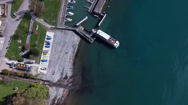 Top down aerial view of passengers boarding and disembarking a ferry on an alpine lake in Switzerland, showing travel and transport activity