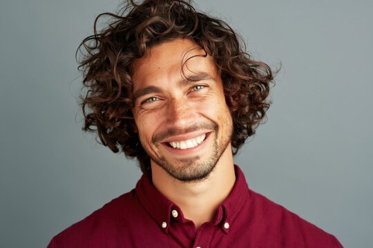 Closeup portrait of smiling man with curly hair and flower against gray background