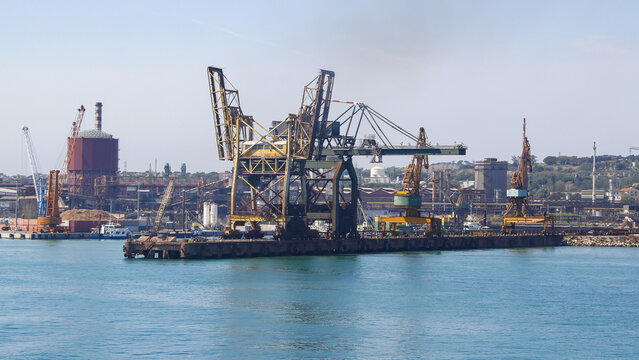View of massive cranes stand sentinel over the harbor where deep blue waters meet industrial might under a clear sky, Piombino, Tuscany, Italy.
