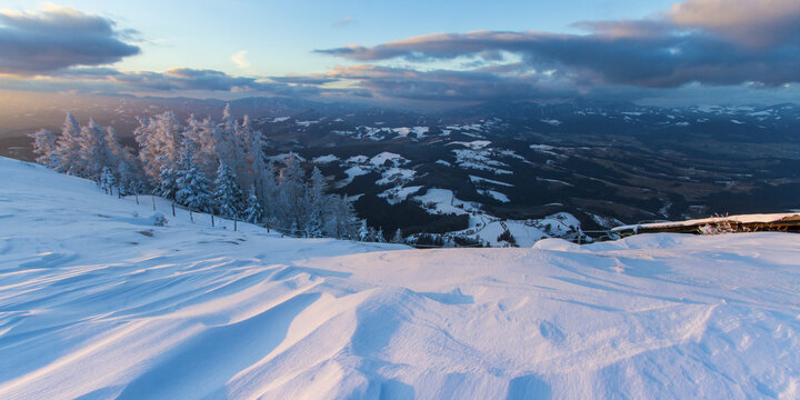 View of snow-laden landscape with frosted trees and a sky painted with dawn's first light, casting shadows on the undulating snowdrifts, Schockl, Styria, Austria.