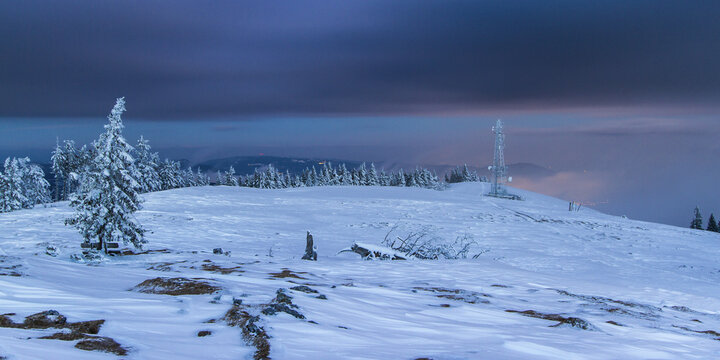View of a snow-covered landscape with frosted trees and a telecommunications tower under a twilight sky, Schockl, Styria, Austria.