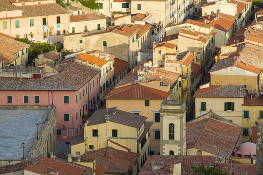 View of sun-kissed terracotta roofs cascade down the hillside, interspersed with pastel buildings, creating a warm, inviting urban landscape, Portoferraio, Elba, Tuscany, Italy.