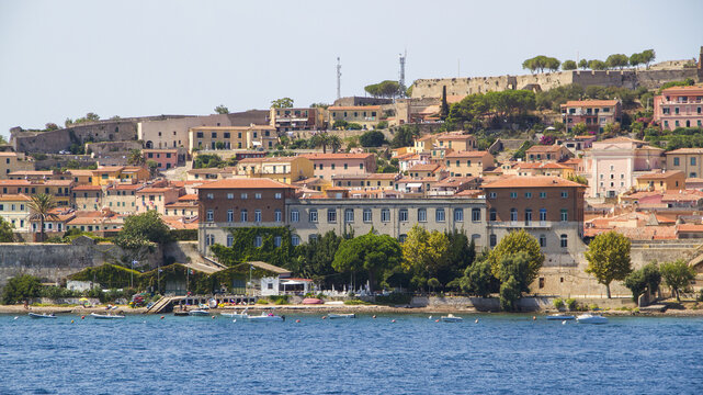 View of the town rising from the azure sea, terracotta roofs and warm stone buildings contrasting with the vibrant blue water, Portoferraio, Elba, Tuscany, Italy.