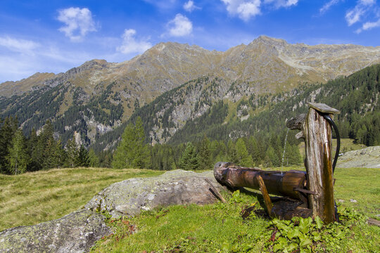 View of a rustic wooden water feature perched on a rocky outcrop, against a backdrop of rugged mountains and lush greenery in Duisitzkarsee, Austria.