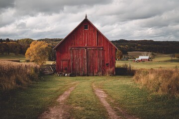 Obraz premium Red barn doors in a tranquil rural farmyard with tree shadows and sunlit grass