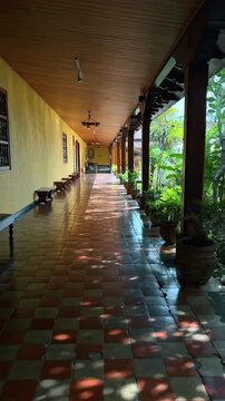 Colonial style corridor with tiled floor and wooden pillars. Long perspective of a traditional architecture walkway with checkered tiles, wooden columns, and potted plants in San Jose.