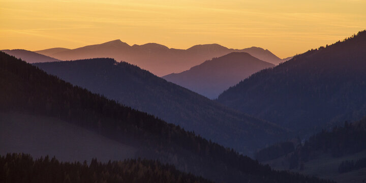 View of layers of blue-tinged mountains fading into the horizon under a soft, golden sky, Sommeralm, Steiermark, Austria.