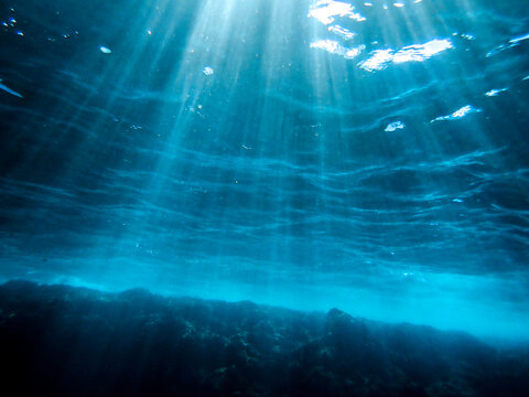 Ocean blue underwater with sunrays, Underwater Sea Deep Water Abstract Sunshine, sea wave , clean waters in summer time, Natural underwater seascape, sand on ocean floor and water surface sunlight.