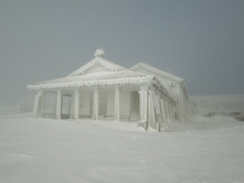 View of a building encased in thick ice stands starkly against the desolate, snow-covered landscape, a testament to winter's harsh grip, Covilha, Distrito da Guarda, Portugal.